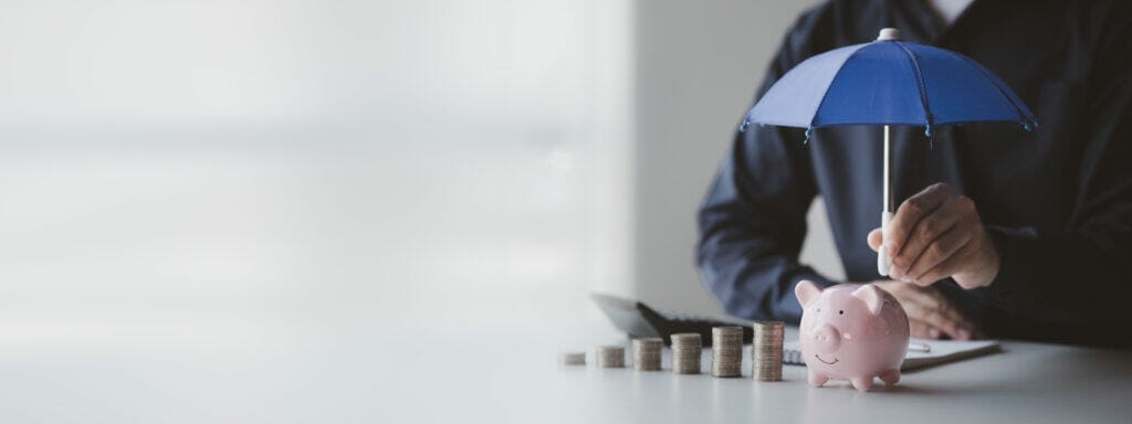 a person spreads a small umbrella on a piggy bank - protect your money concept