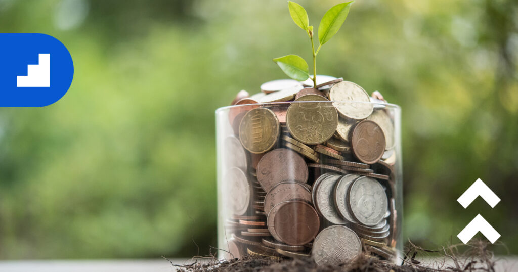 Glass jar filled with assorted coins with a small green plant sprouting from the top, symbolizing financial growth.