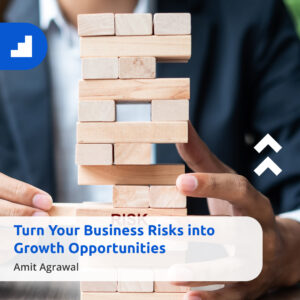 Close-up of a person in a business suit carefully pulling a wooden block from a Jenga tower, symbolizing managing business risks and turning them into growth opportunities. Text overlay reads: ‘Turn Your Business Risks into Growth Opportunities –Amit Agrawal.’