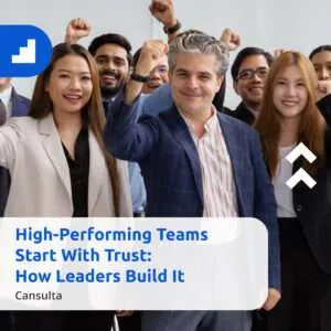 A diverse group of professional team members smiling and raising their fists in celebration, standing behind a banner that reads ‘High-Performing Teams Start With Trust: How Leaders Build It – Cansulta