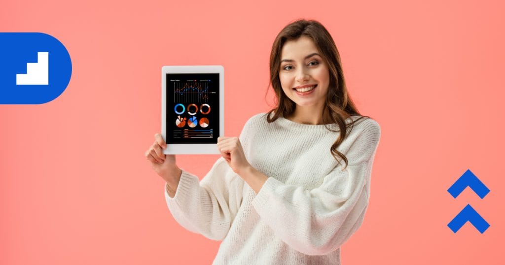 A smiling woman stands against a pink background, holding a tablet that displays charts and graphs, representing data analysis, measurement, and reporting.