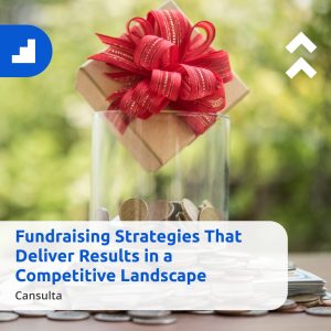 A glass jar filled with coins topped with a gift box tied with a red ribbon, set against a blurred green outdoor background. Overlaid text reads “Fundraising Strategies That Deliver Results in a Competitive Landscape,” with the name “Cansulta” shown below, representing effective and impactful fundraising efforts.
