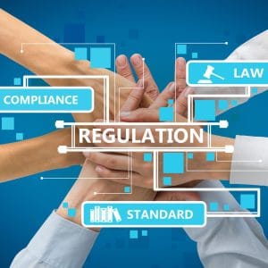Multiple hands stacked together in a team unity gesture overlaid with a digital graphic interface featuring the words "Regulation" at the center, surrounded by labeled icons for "Law," "Compliance," and "Standard" against a blue technological background, symbolizing collective commitment to regulatory compliance.