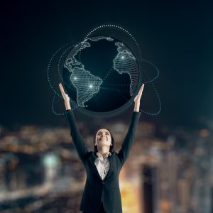 A businesswoman looks up and raises her hands toward a glowing, digital globe encircled by data connection lines, symbolizing global connectivity and international business strategy.