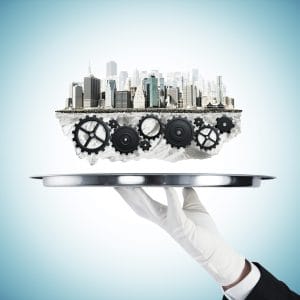 A hand in a white glove holds a silver platter, upon which a miniature city skyline floats above a system of interconnected black gears embedded in a rocky foundation.