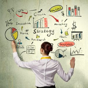 A businesswoman, seen from behind, drawing an intricate business strategy plan—complete with charts, diagrams, a SWOT analysis, and the word 'Strategy'—on a textured wall.