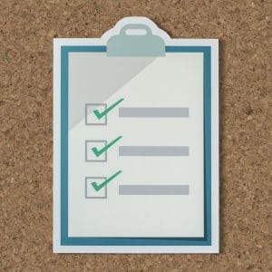 A flat-lay illustration of a white and teal clipboard featuring a checklist with three green checkmarks next to gray text lines, set against a textured cork board background, representing completion, tasks, and organization