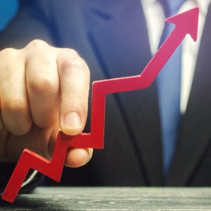 Close-up of a person in a business suit holding a jagged red wooden arrow pointing upward, symbolizing continuous business growth, increasing revenue, and upward performance trends